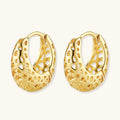 Close-up of small gold-plated hoop earrings with intricate honeycomb cutout pattern on cream background.
